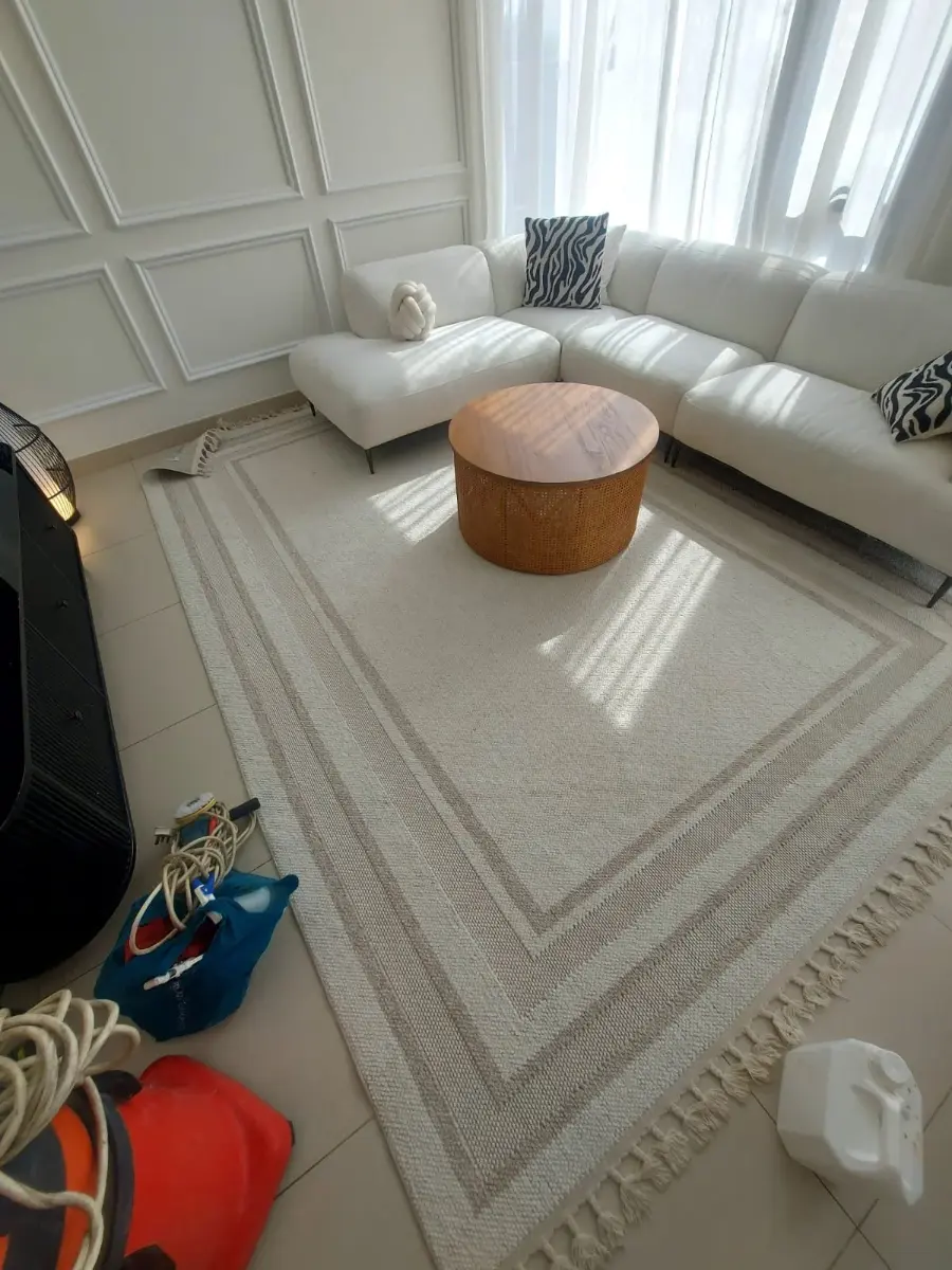 Living room with white sofas and a rug set up for a deep cleaning job in a Dubai villa, with cleaning equipment on the floor